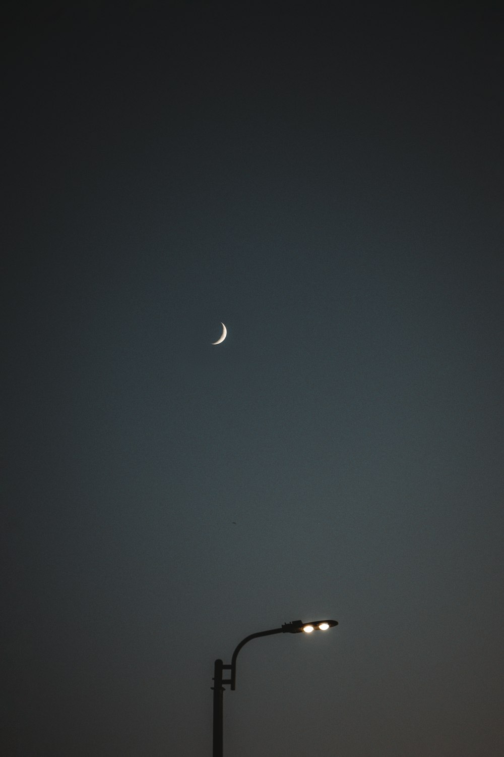 a street light with a half moon in the sky