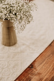 Close-up of pastel-colored crochet flowers arranged in a light beige vase on a wooden table.