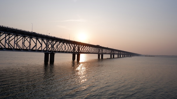 A composite bridge spanning a wide river, captured during sunset with warm light reflecting off its surfaces.