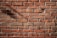 Red bricks are arranged in a tightly knit pattern, showing both the texture and mortar lines clearly. The surface is well-lit, emphasizing the rough texture and natural color variations found in the bricks. Some shadows are cast across the bricks, adding depth to the flat surface.
