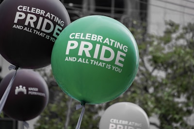 Large balloons with messages celebrating pride float in an outdoor environment, surrounded by greenery.