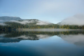 A serene nature shot featuring morning mist over a calm lake.