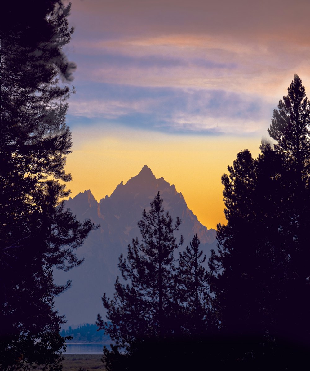 the sun is setting behind the mountains and trees