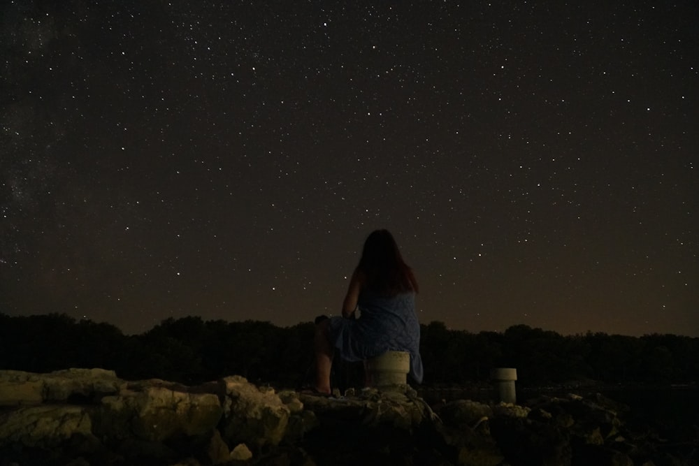a woman sitting on a rock looking up at the stars