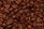 A close-up view of a heap of roasted coffee beans. The beans exhibit a rich, dark brown color and have a shiny, oily surface. Each bean is distinct, with visible textures and creases characteristic of roasted coffee beans.