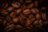 Close-up of glossy coffee beans with golden light reflections on a matte black surface.