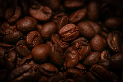 Close-up of glossy coffee beans with golden light reflections on a matte black surface.