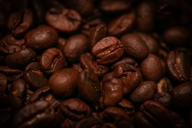 Close-up view of several roasted coffee beans, showcasing their rich brown texture and glossy surface. The lighting highlights the deep creases and curves of the beans, giving them a warm and inviting appearance.