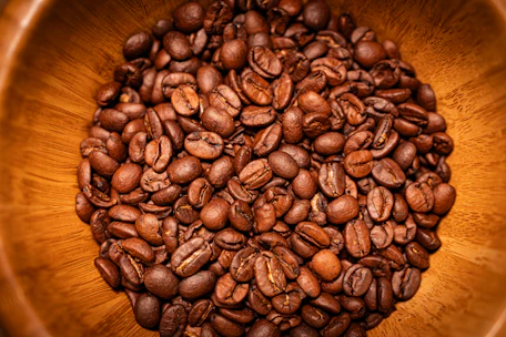 Close-up of raw green coffee beans in a rustic wooden bowl.