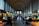 A grand library hall with tall arched windows and elaborate moldings on the ceiling. Rows of large wooden tables are lined with green reading lamps, and people are seated, engaged in reading or using laptops. The shelves are filled with numerous books, and the ambiance is quiet and studious.