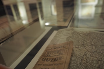 A display case with old maps and a vintage pamphlet titled 'Pathfinder Railway Guide' showing intricate details of streets and regions.