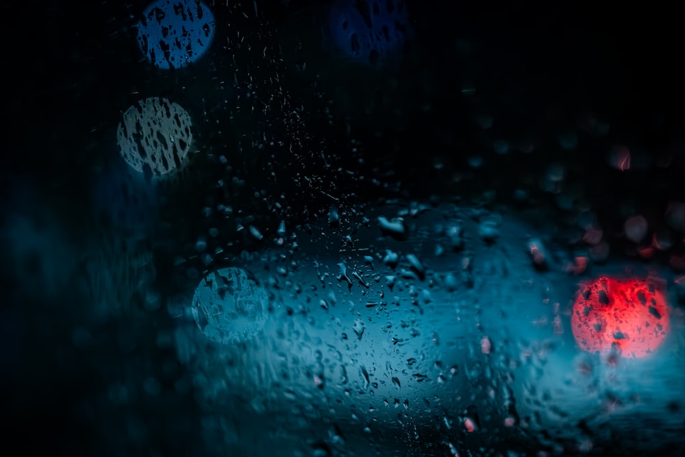 un parabrisas cubierto de lluvia con una luz de freno roja en el fondo