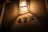 A dimly lit wall with the number 475 displayed in metal numbers beneath a glowing, vintage-style lantern. The soft, warm light casts shadows and highlights the textured wall surface. There are small flowers appearing in the top left corner, adding a subtle touch of nature.