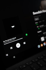 A close-up view of a digital screen displaying a music player interface. The screen shows controls for playing music, including a play/pause button, volume, and track information. The display is dark with a minimalistic design.