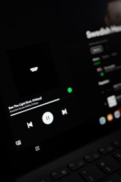 A close-up view of a digital screen displaying a music player interface. The screen shows controls for playing music, including a play/pause button, volume, and track information. The display is dark with a minimalistic design.