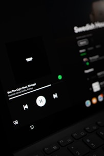 A close-up view of a digital screen displaying a music player interface. The screen shows controls for playing music, including a play/pause button, volume, and track information. The display is dark with a minimalistic design.