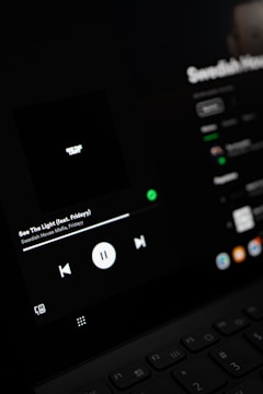 A close-up view of a digital screen displaying a music player interface. The screen shows controls for playing music, including a play/pause button, volume, and track information. The display is dark with a minimalistic design.