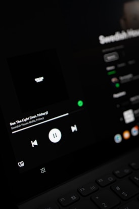 A close-up view of a digital screen displaying a music player interface. The screen shows controls for playing music, including a play/pause button, volume, and track information. The display is dark with a minimalistic design.