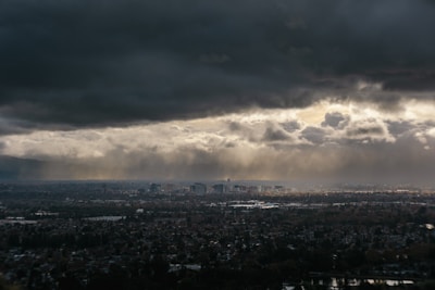 A sprawling futuristic city enclosed by massive walls under a dark, stormy sky with faint glimpses of otherworldly creatures beyond.