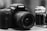 A close-up view of two cameras, one prominently in the foreground and one partially visible in the background. The foreground camera has a large lens and notable branding on top.