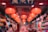 A vibrant shop interior illuminated by a series of red lanterns hanging from the ceiling. The shop is filled with a variety of colorful items and decorations, arranged neatly on shelves. Two people are present, one appearing to browse the merchandise.