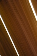 Several dark wooden panels are aligned diagonally with narrow strips of bright white lighting in between them, creating a sleek and modern appearance.