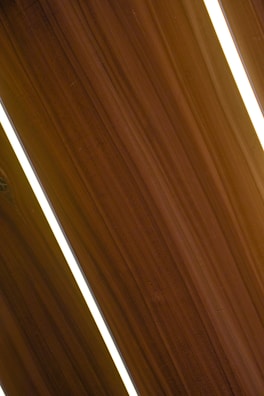 Several dark wooden panels are aligned diagonally with narrow strips of bright white lighting in between them, creating a sleek and modern appearance.