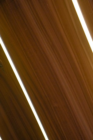 Several dark wooden panels are aligned diagonally with narrow strips of bright white lighting in between them, creating a sleek and modern appearance.