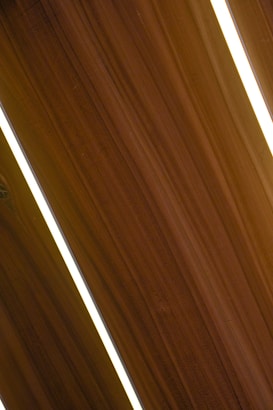 Several dark wooden panels are aligned diagonally with narrow strips of bright white lighting in between them, creating a sleek and modern appearance.