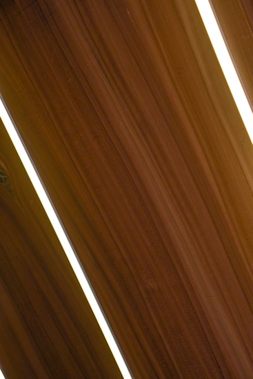 Several dark wooden panels are aligned diagonally with narrow strips of bright white lighting in between them, creating a sleek and modern appearance.