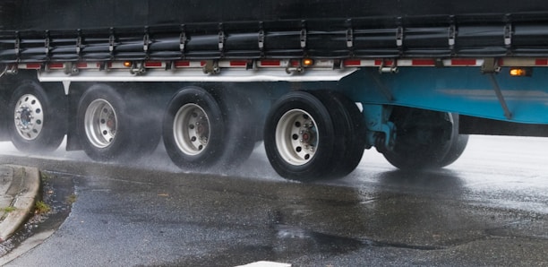 Close-up black and white image of a truck's heavy-duty tires rolling over a wet road.