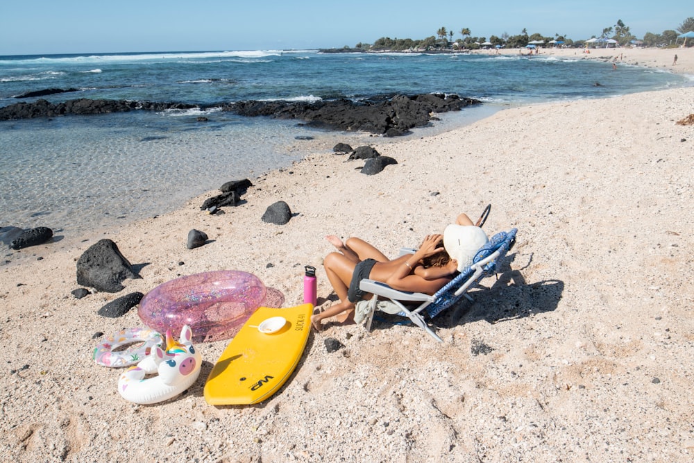 una mujer sentada en una silla en una playa junto a un cuerpo de agua