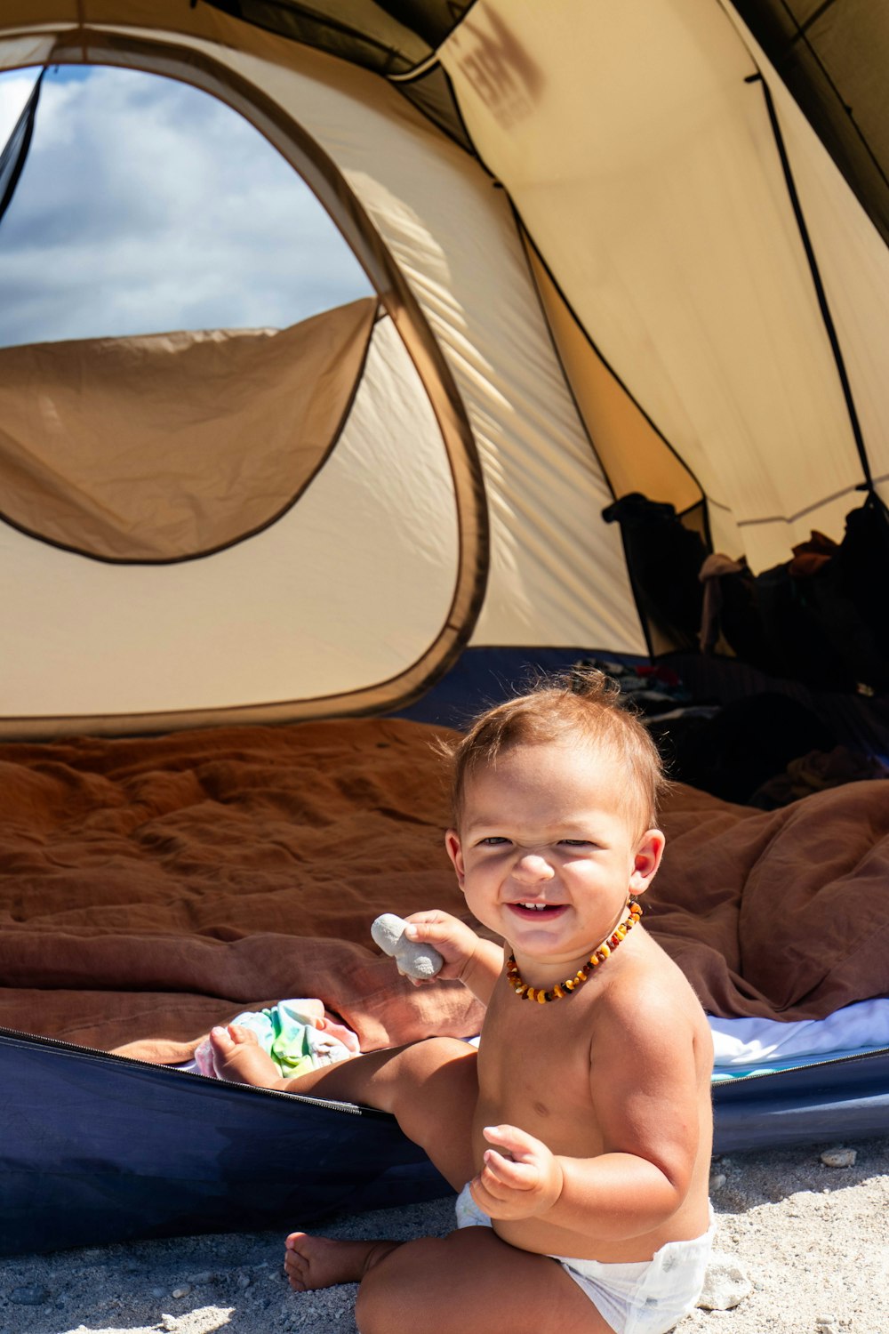 a baby in a diaper playing with a toothbrush in front of a tent