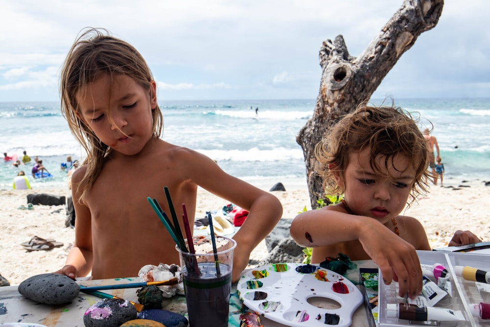 two children sitting at a table on the beach
