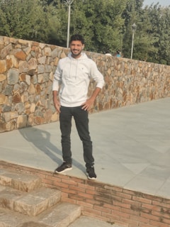A man wearing a navy blue hoodie with a front pocket, standing against a brick wall.