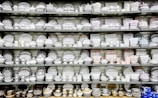 A collection of white and patterned china dishes, including plates, bowls, cups, and saucers, is neatly arranged on several shelves. The china features various intricate designs and colors, showcasing a wide range of styles.