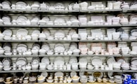 A collection of white and patterned china dishes, including plates, bowls, cups, and saucers, is neatly arranged on several shelves. The china features various intricate designs and colors, showcasing a wide range of styles.