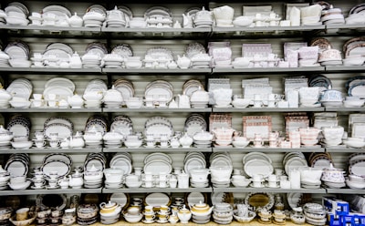 A collection of white and patterned china dishes, including plates, bowls, cups, and saucers, is neatly arranged on several shelves. The china features various intricate designs and colors, showcasing a wide range of styles.