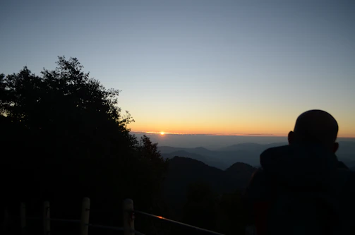 Sunset silhouette of a traveler admiring a scenic mountain view.
