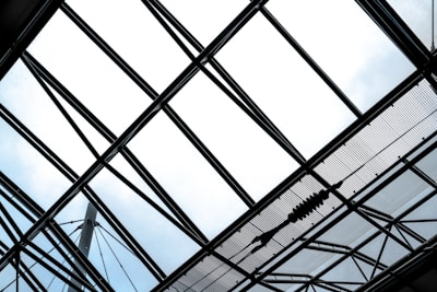 A geometric framework of steel beams and glass panes forms a large, intricate pattern against the sky. The structure creates a crisscrossed grid, with individual sections allowing light to pass through.