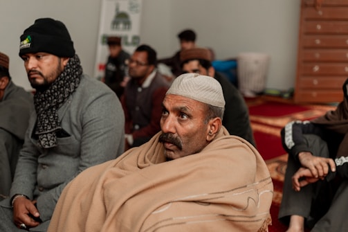 A group of Aimaq elders discussing community development plans around a traditional Afghan rug.