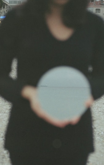 A person is holding a reflective sphere, capturing an image of an overcast sky and a distant body of water. The individual and their surroundings are blurred, placing focus on the sphere's reflection.