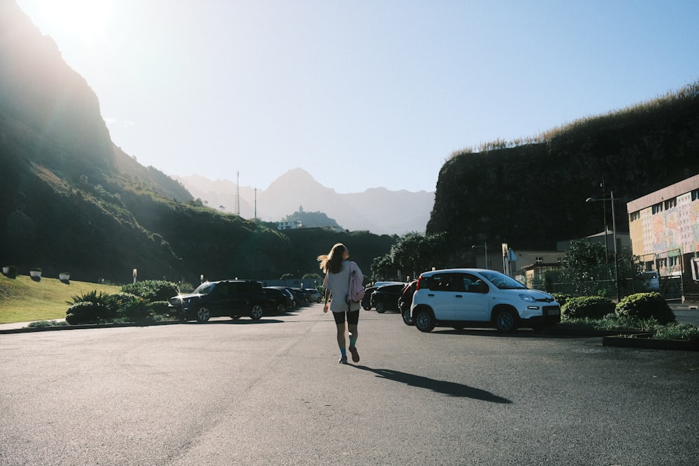 a woman walking across a parking lot next to parked cars