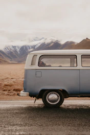 A candid photo of Eva and Andrés driving their iconic blue van on a scenic road surrounded by mountains.