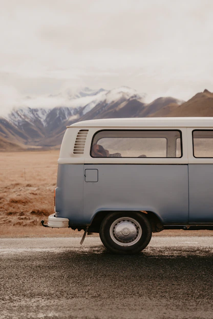 A candid photo of Eva and Andrés driving their iconic blue van on a scenic road surrounded by mountains.