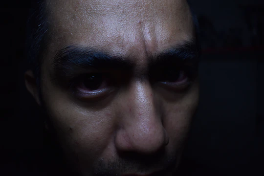 A close-up of a person’s determined face illuminated by dim light, beads of sweat visible as they push through a tough challenge.
