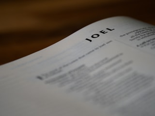 A close-up of a page from a book with the name 'Joel' prominently displayed at the top. The text on the page is blurred except for the name, suggesting a biblical context or a title page.