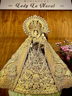 A delicate vase with religious engravings resting beside a small statue of a saint.