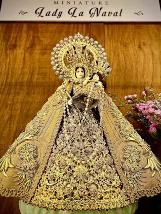 A delicate vase with religious engravings resting beside a small statue of a saint.