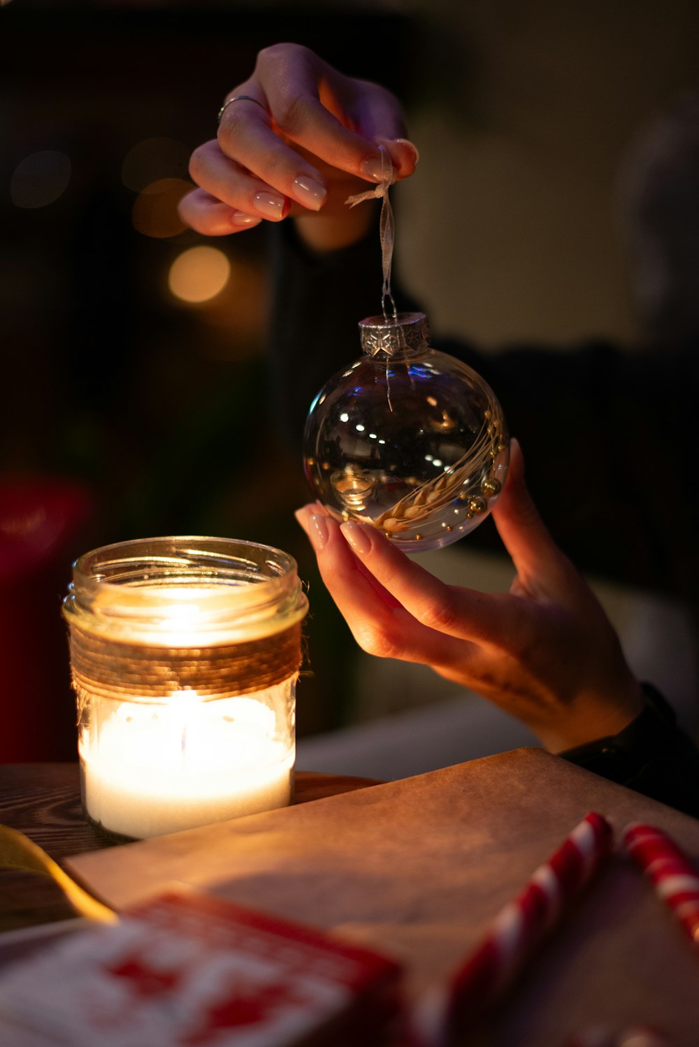 a person holding a glass ornament over a jar of candy canes